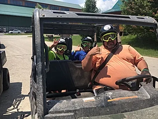 A man is driving a vehicle with two children in it.