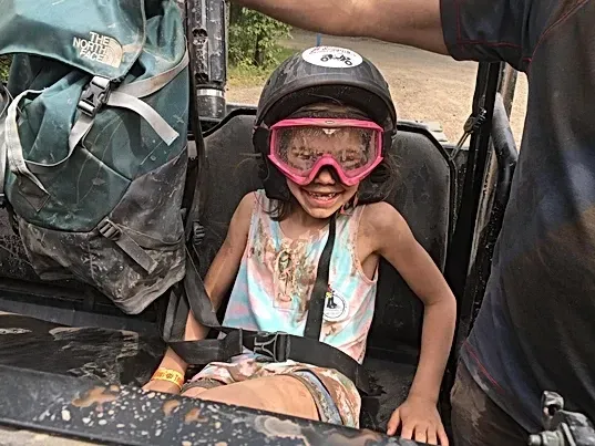 A little girl wearing a helmet and goggles is sitting in a vehicle.