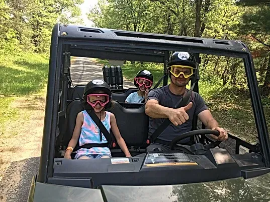 A man and two children are riding in a atv on a dirt road.