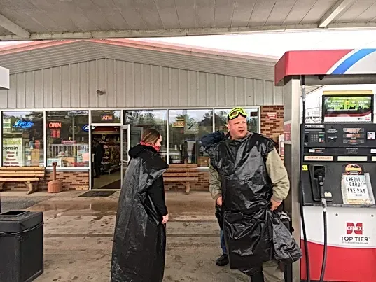 A man and a woman are standing in front of a gas pump at a gas station.