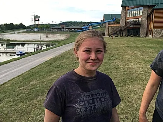 A woman in a purple shirt is standing in front of a building.