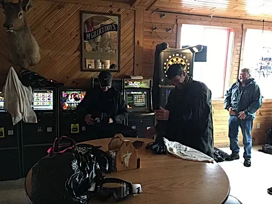 Two men are sitting at a table in a room with a deer head on the wall.