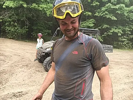 A man wearing a helmet and goggles is standing in a dirt field.