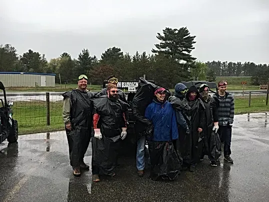 A group of people are standing in front of a vehicle in the rain.