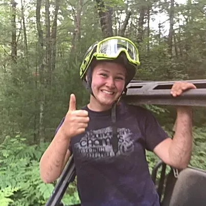 A woman wearing a helmet and goggles is giving a thumbs up.