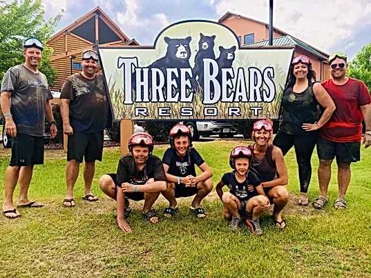 A group of people are posing for a picture in front of a three bears resort sign.