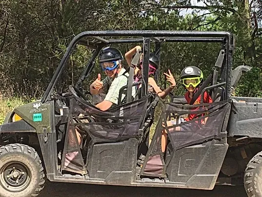 A man and two children are riding in a four wheeler.