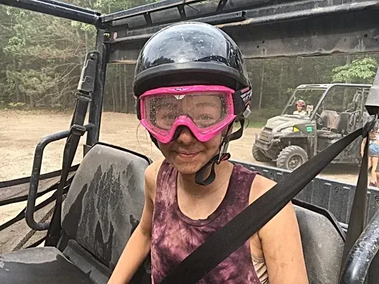 A young girl wearing a helmet and goggles is sitting in a vehicle.