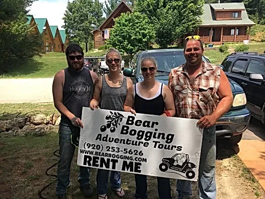 A group of people holding a sign that says `` bear bogging adventure tours rent me ''.