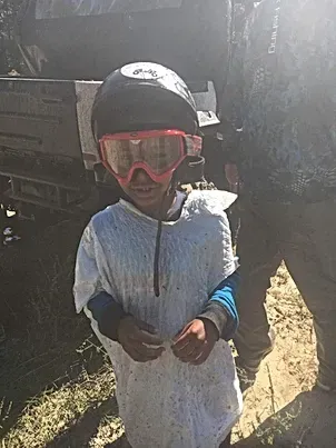 A young boy wearing a helmet and goggles is standing in front of a truck.