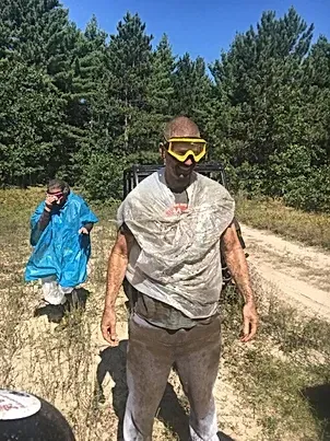A man wearing goggles and a plastic bag is standing in a field.