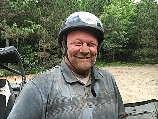 A man wearing a helmet and a dirty shirt is smiling.