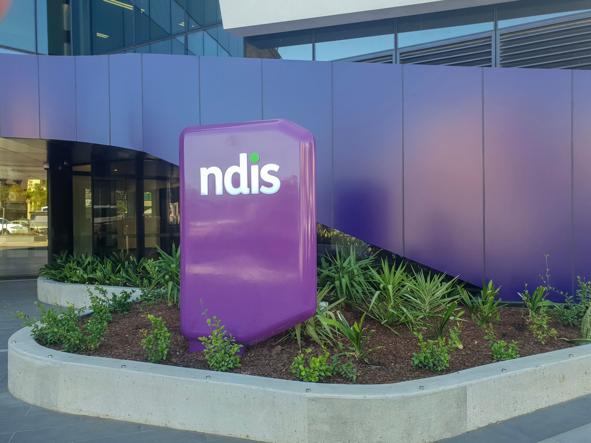 Purple NDIS sign in front of a modern building and landscaped planter bed