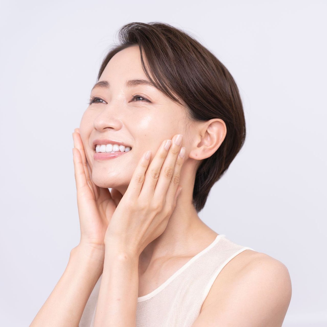 A woman is smiling and touching her face with her hands.