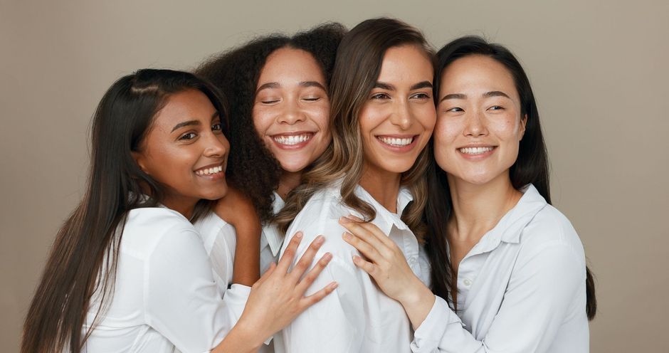 A woman is smiling and touching her neck with her hand.