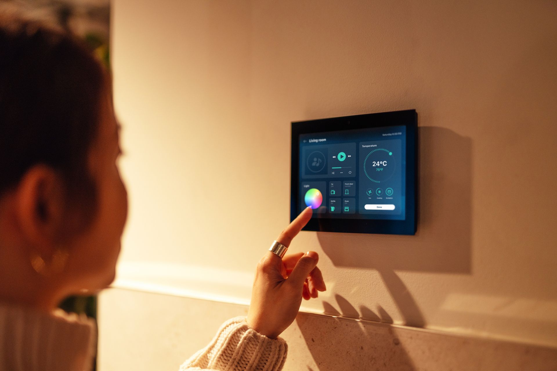 A woman is using a smart thermostat on a wall.