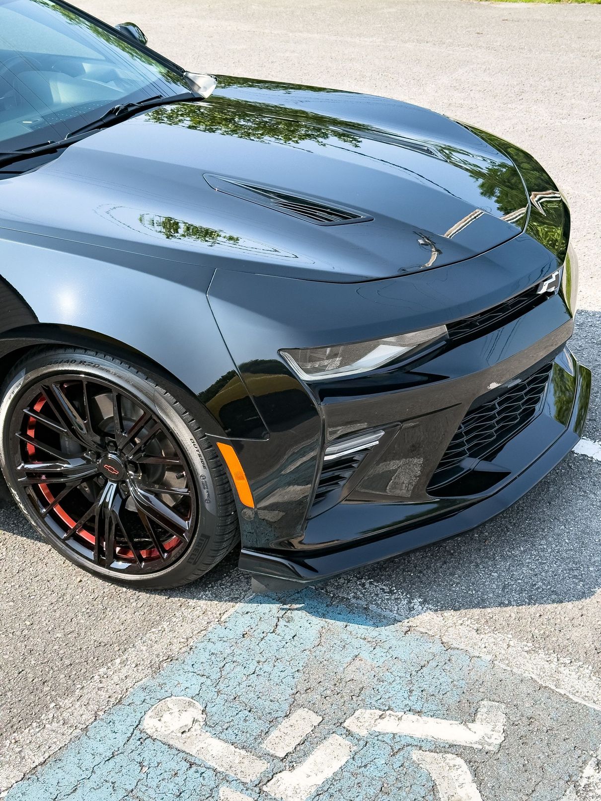 Black Chevrolet Camaro parked over a blue and white handicap symbol on pavement.