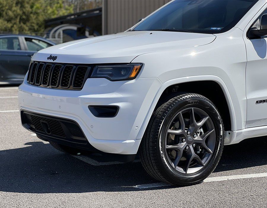 White Jeep Grand Cherokee SUV parked outdoors, with black grill and dark gray wheels.