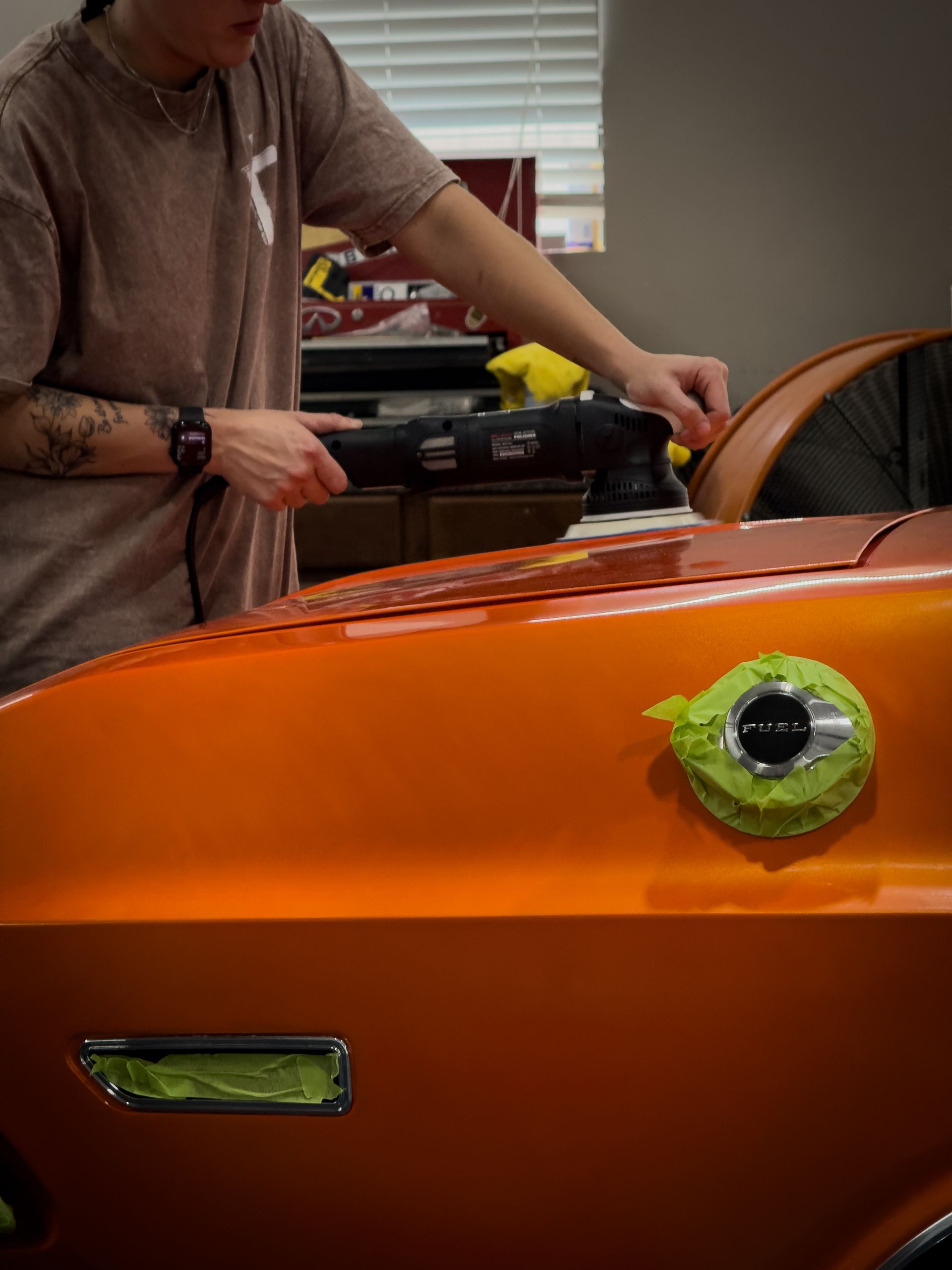 Person polishing an orange classic car with a power buffer.