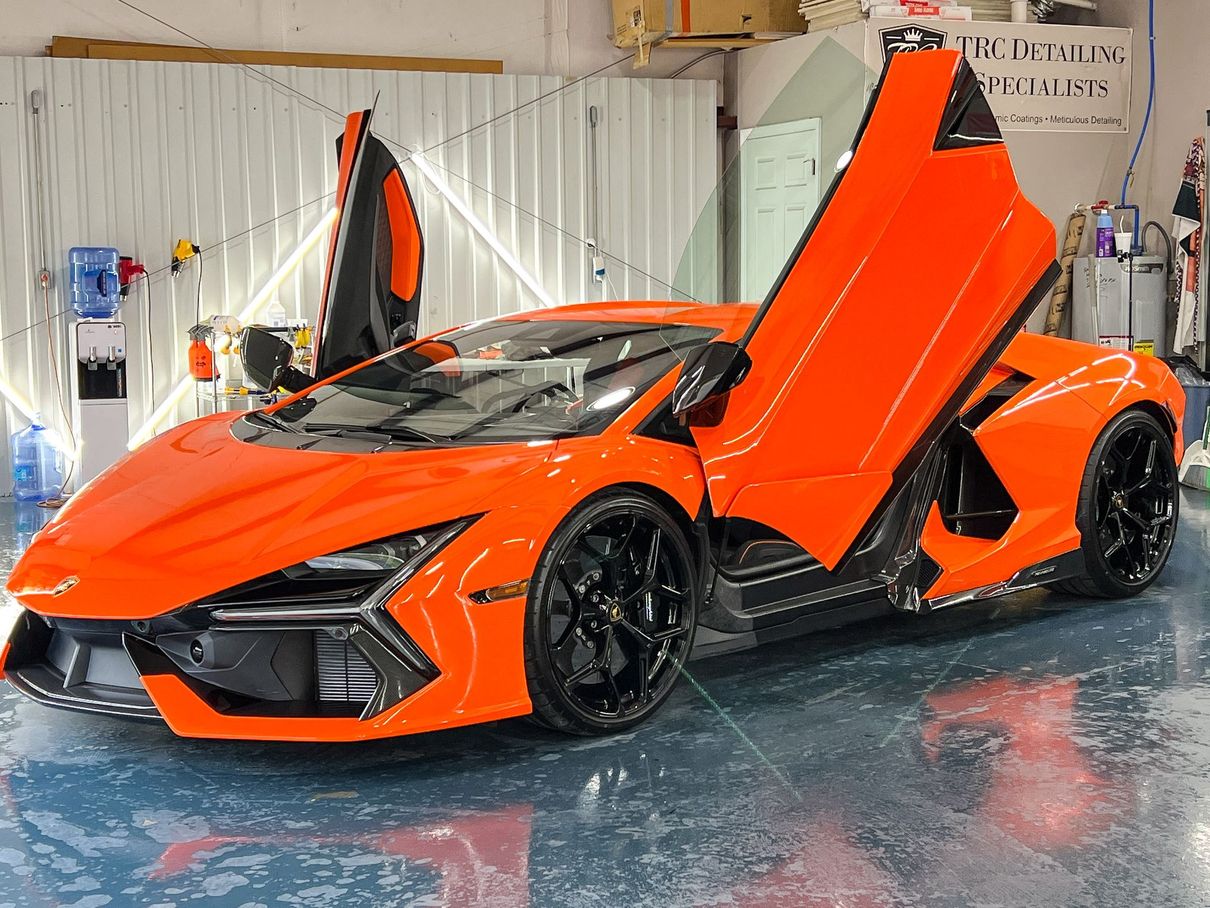 Orange Lamborghini with black wheels, doors open, parked inside a garage.