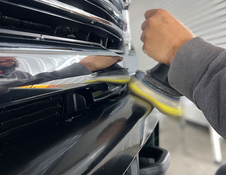 Person polishing a black car bumper with a power buffer.