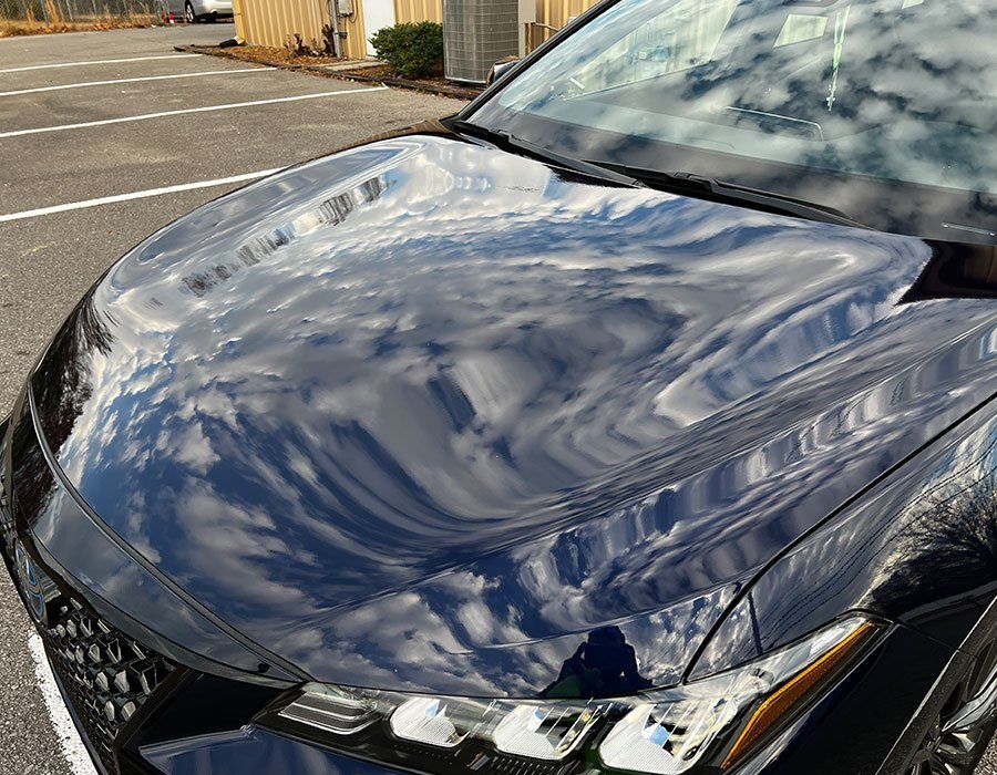 Black car hood reflects sky and clouds.