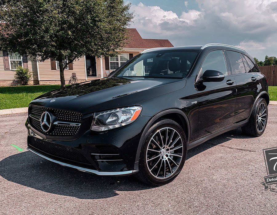 Black Mercedes-Benz SUV parked on a paved road in front of a house on a sunny day.