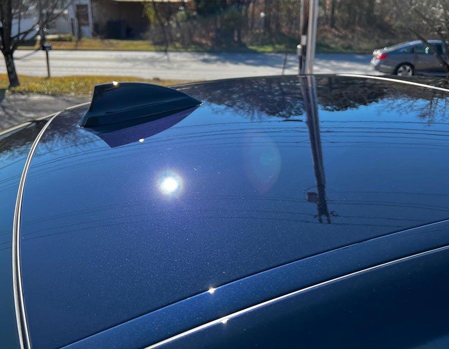 Blue car roof with fin antenna reflecting the bright sun.