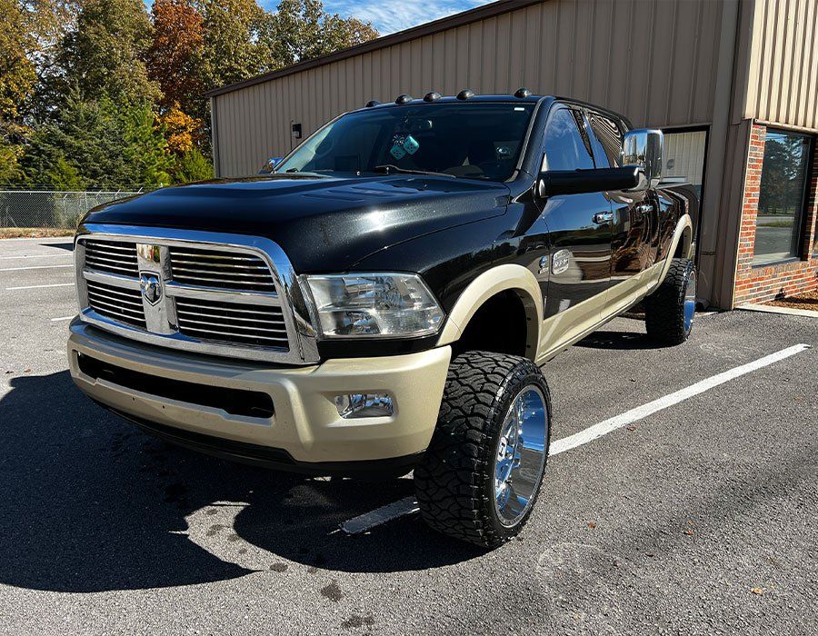 Black and tan Ram pickup truck parked in a lot, shiny wheels, and building in the background.