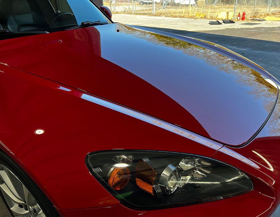 Red Honda S2000 car hood with shiny, reflective finish and black headlight.