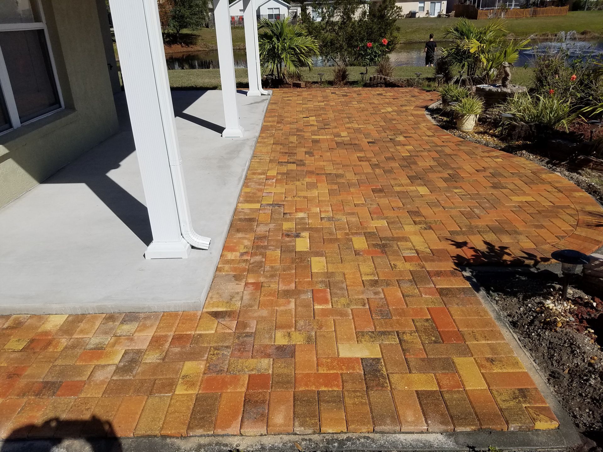 Brick patio extending from a light-colored building with white columns. The brick is a mix of red and yellow tones.