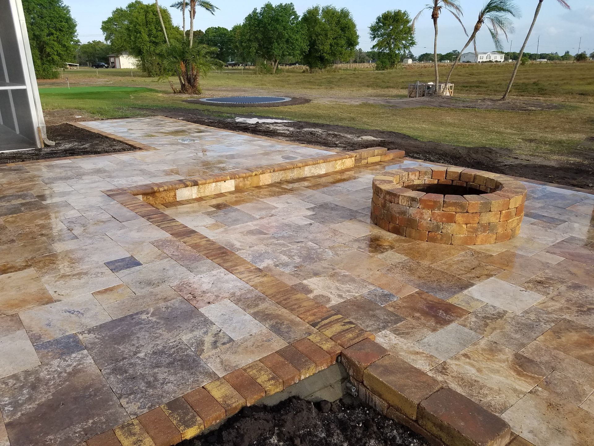 Patio with stone pavers and a brick fire pit, bordered by brick detailing. Setting outdoors in a grassy area.