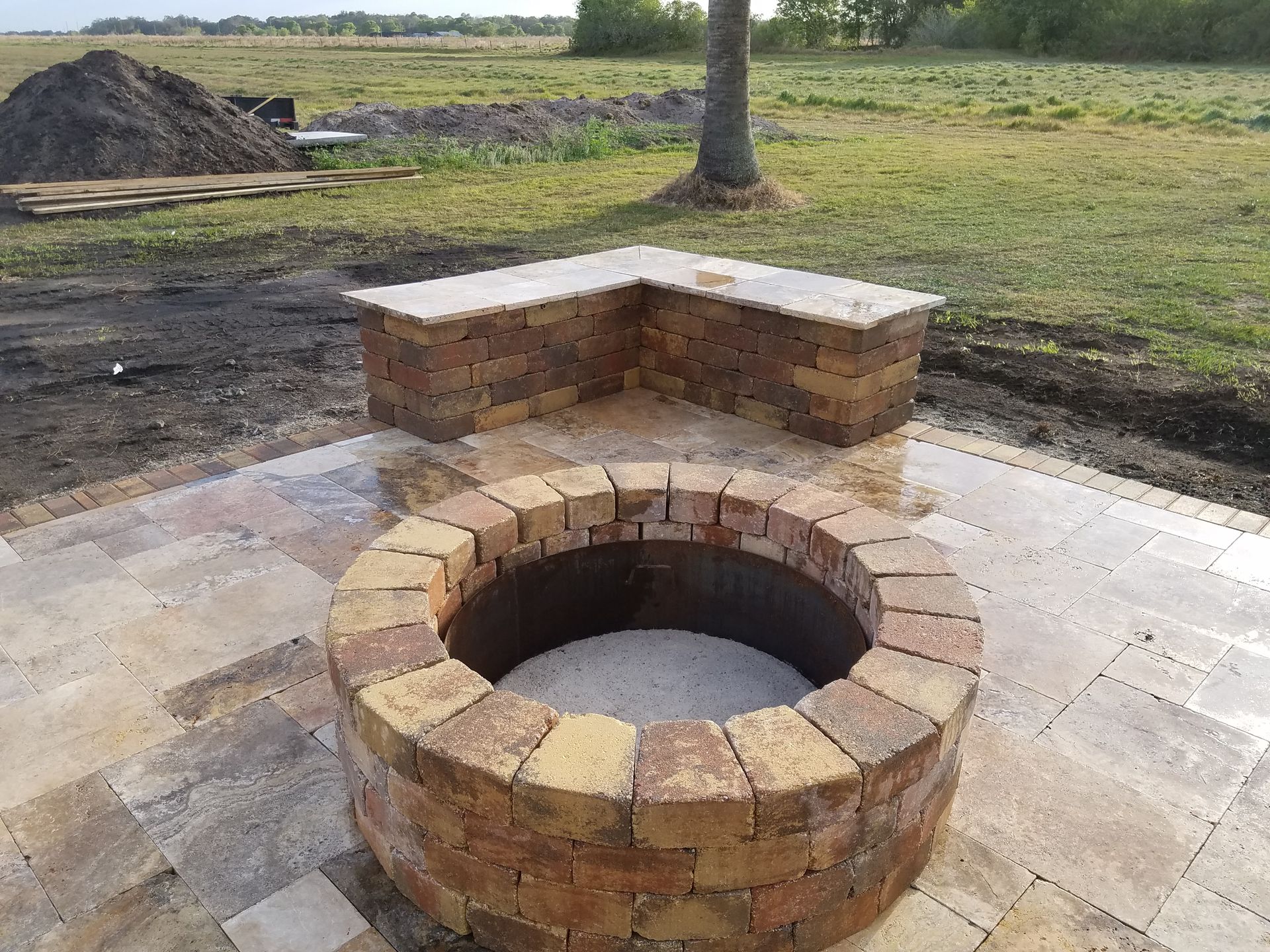 An outdoor fire pit and seating area. A round brick fire pit sits on a paved patio with a brick bench.