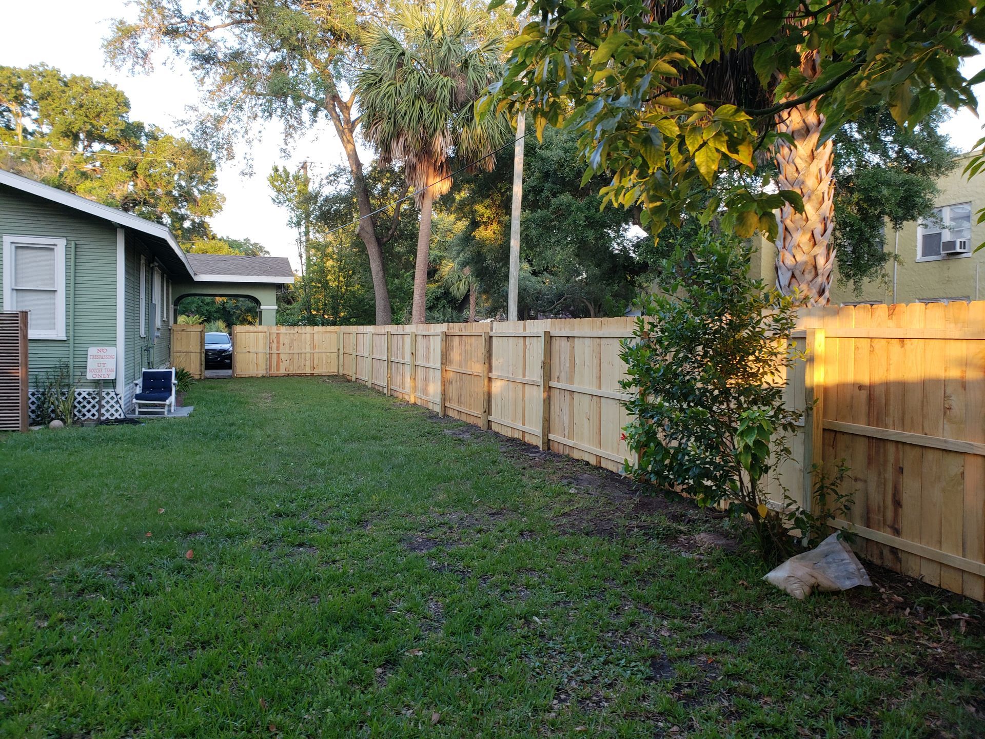 A backyard with green grass, a new wooden fence, and a small house on a sunny day.