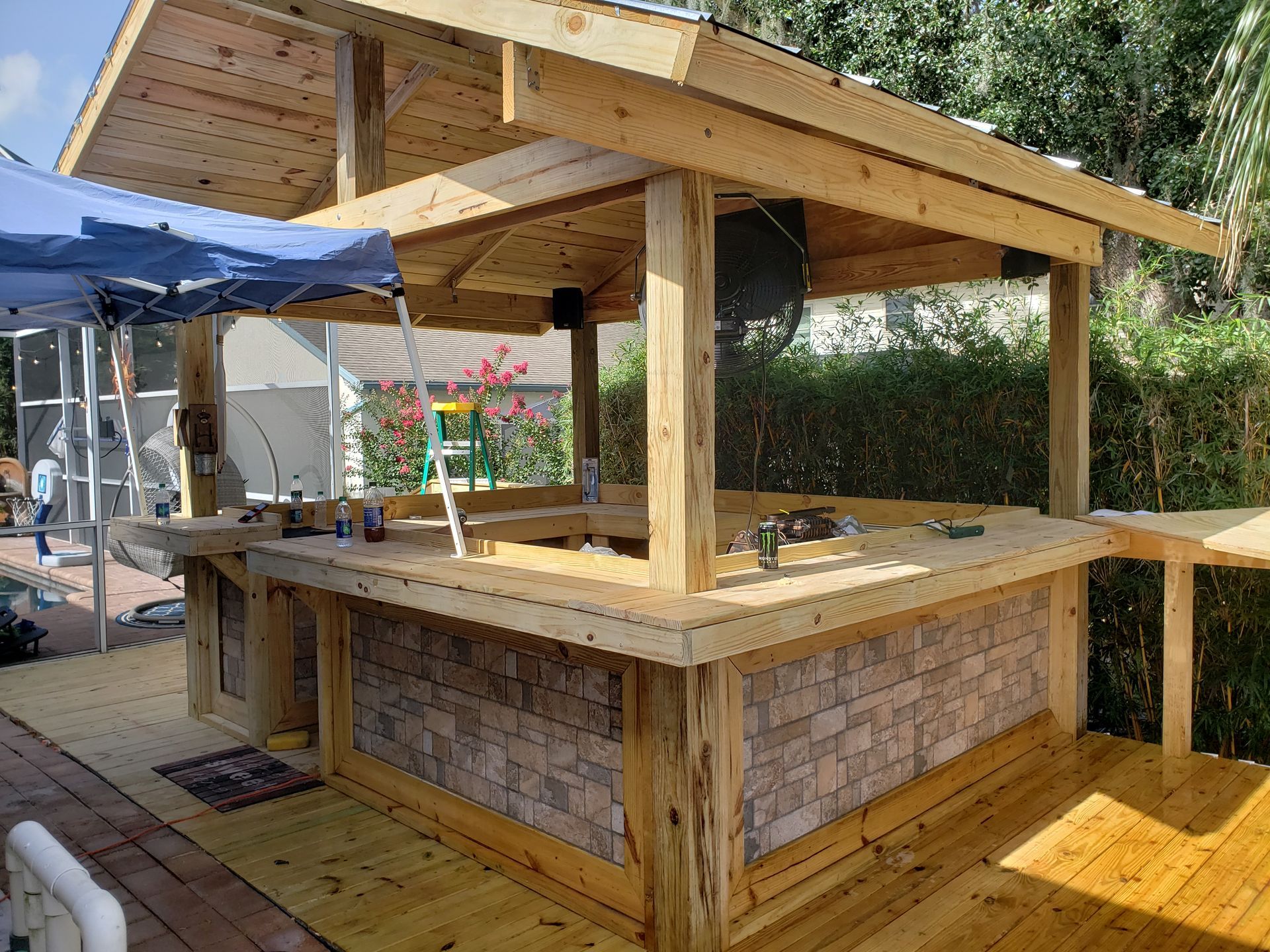 Wooden outdoor bar under construction, featuring a stone veneer front, on a wooden deck.