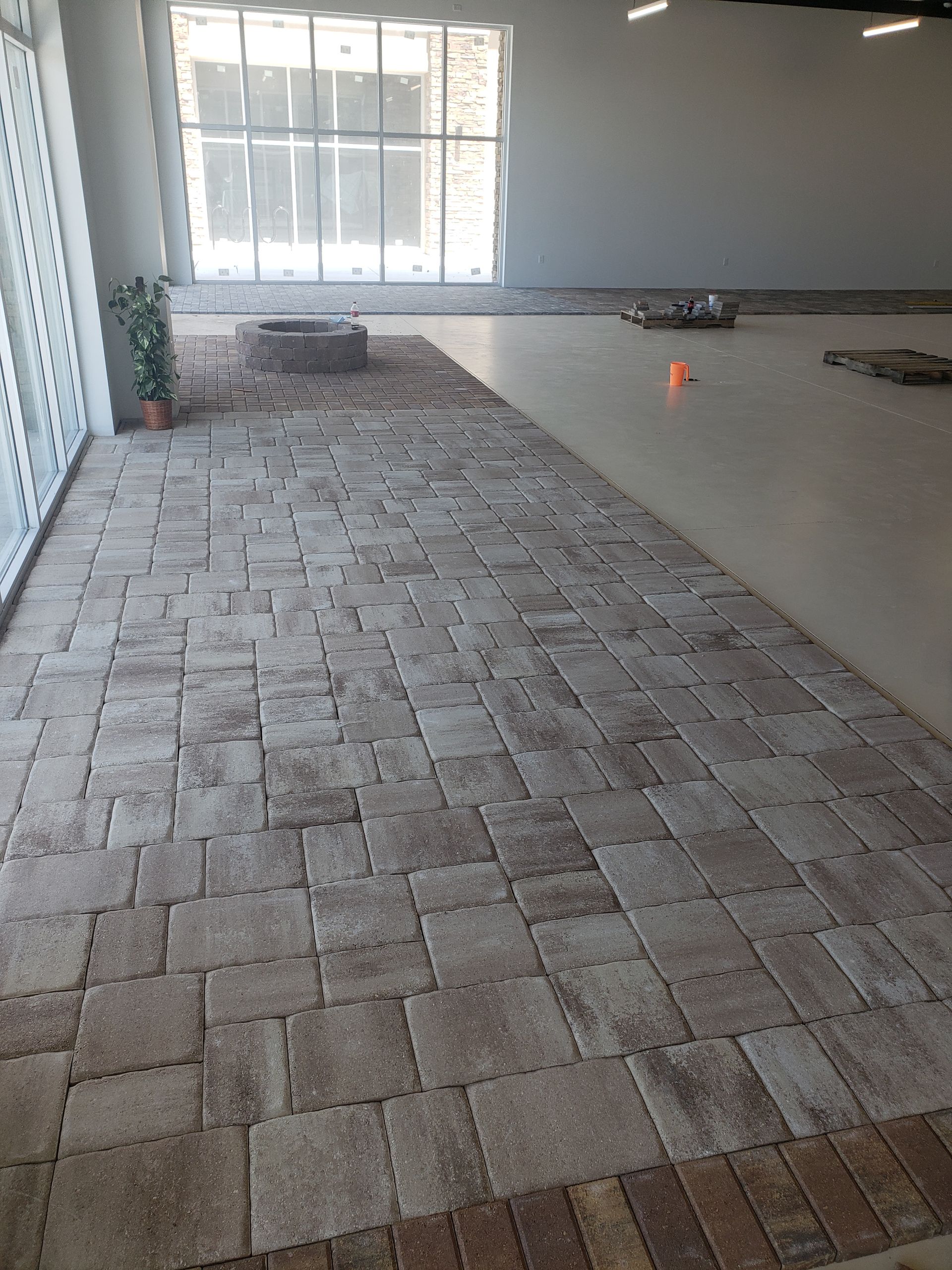 Room with brick pavers extending from a glass door, leading to a concrete floor. In the background is a window and a fire pit.