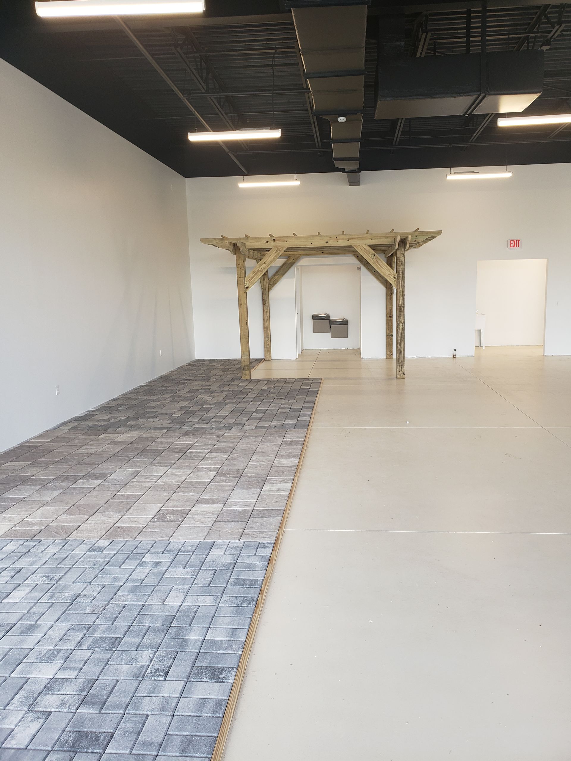 A large open room with a two-toned floor: one side is patterned gray tiles, the other is light beige. A wooden structure stands in the center.