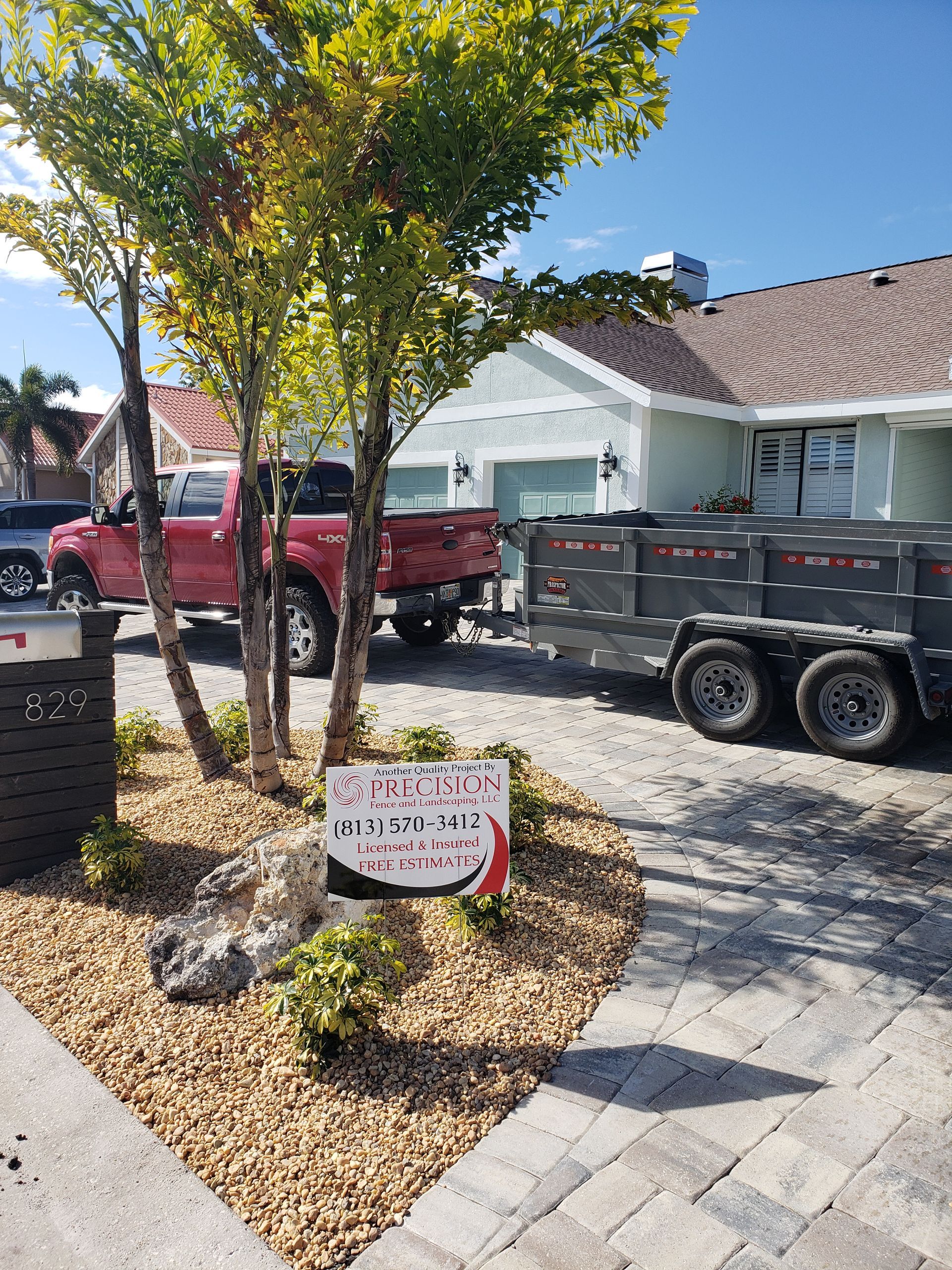A red truck and trailer parked in front of a house with a landscaping business sign.