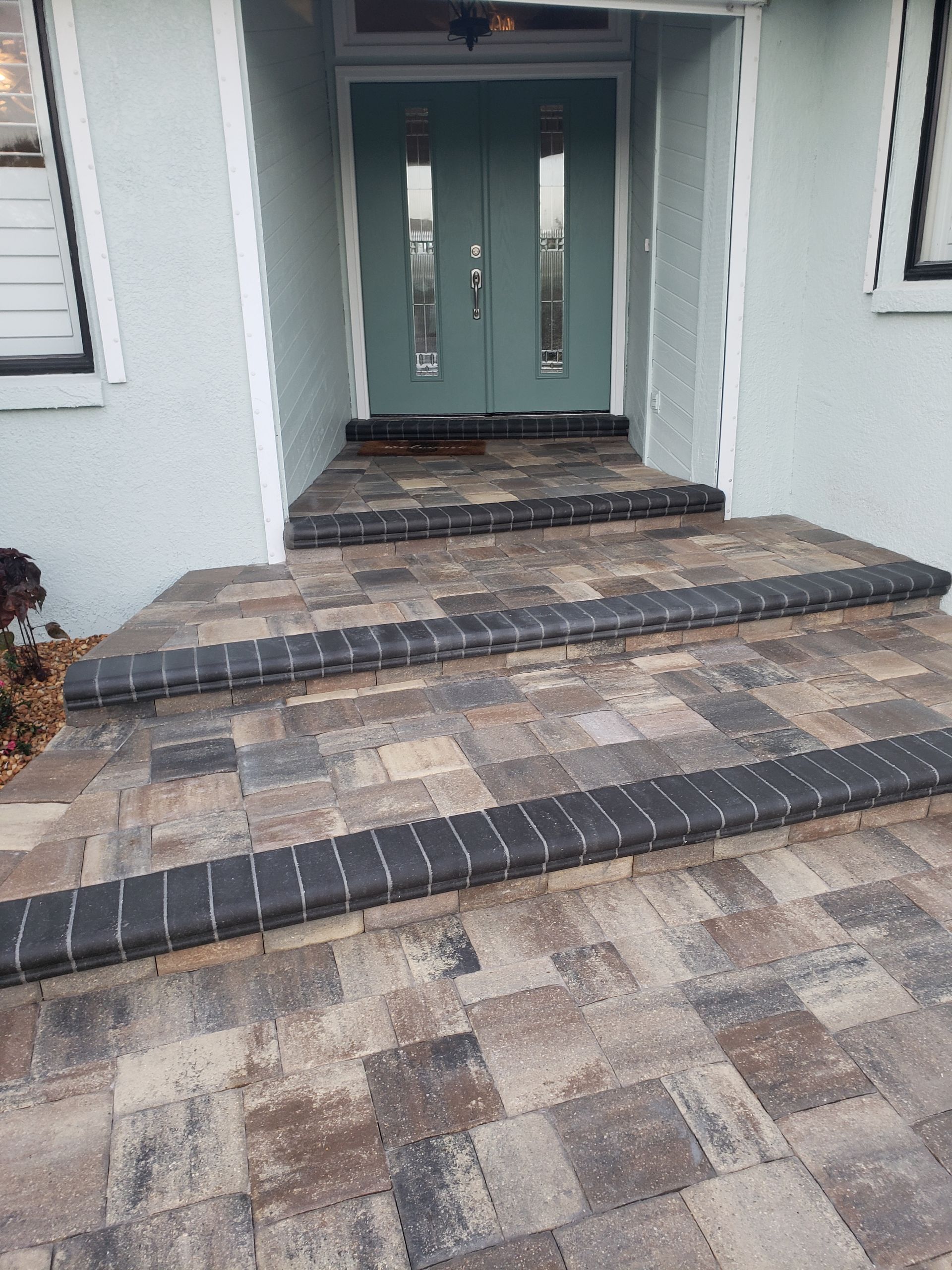 Brick walkway and steps leading to a teal front door. The steps are trimmed with dark brick borders, with a light blue house exterior.