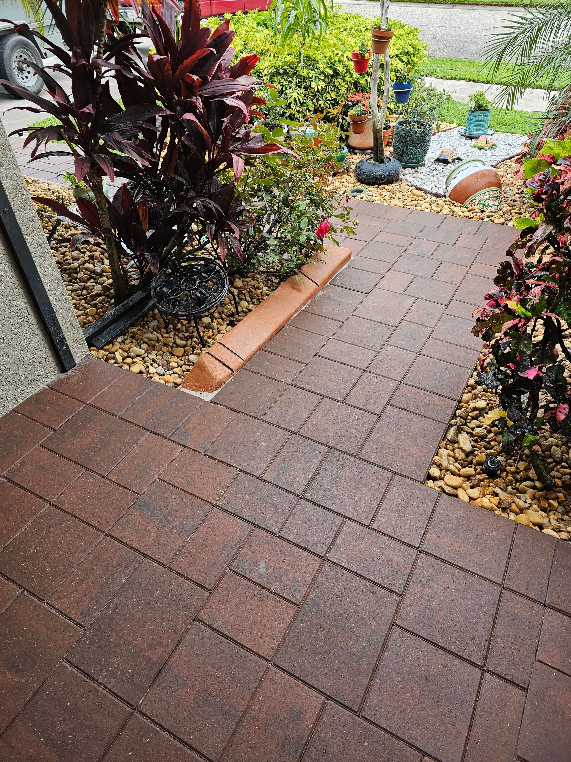 Brick pathway leads to a front door, surrounded by landscaping with red and green plants and brown mulch.