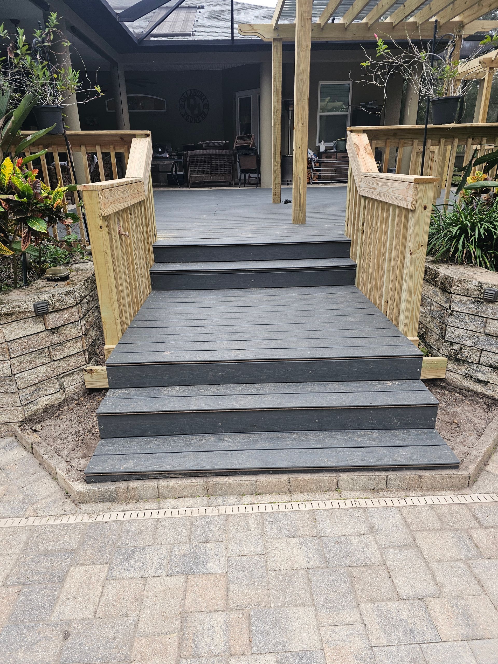 Steps leading up to a raised deck with wooden railings and a pergola. Steps are covered in gray shingles.