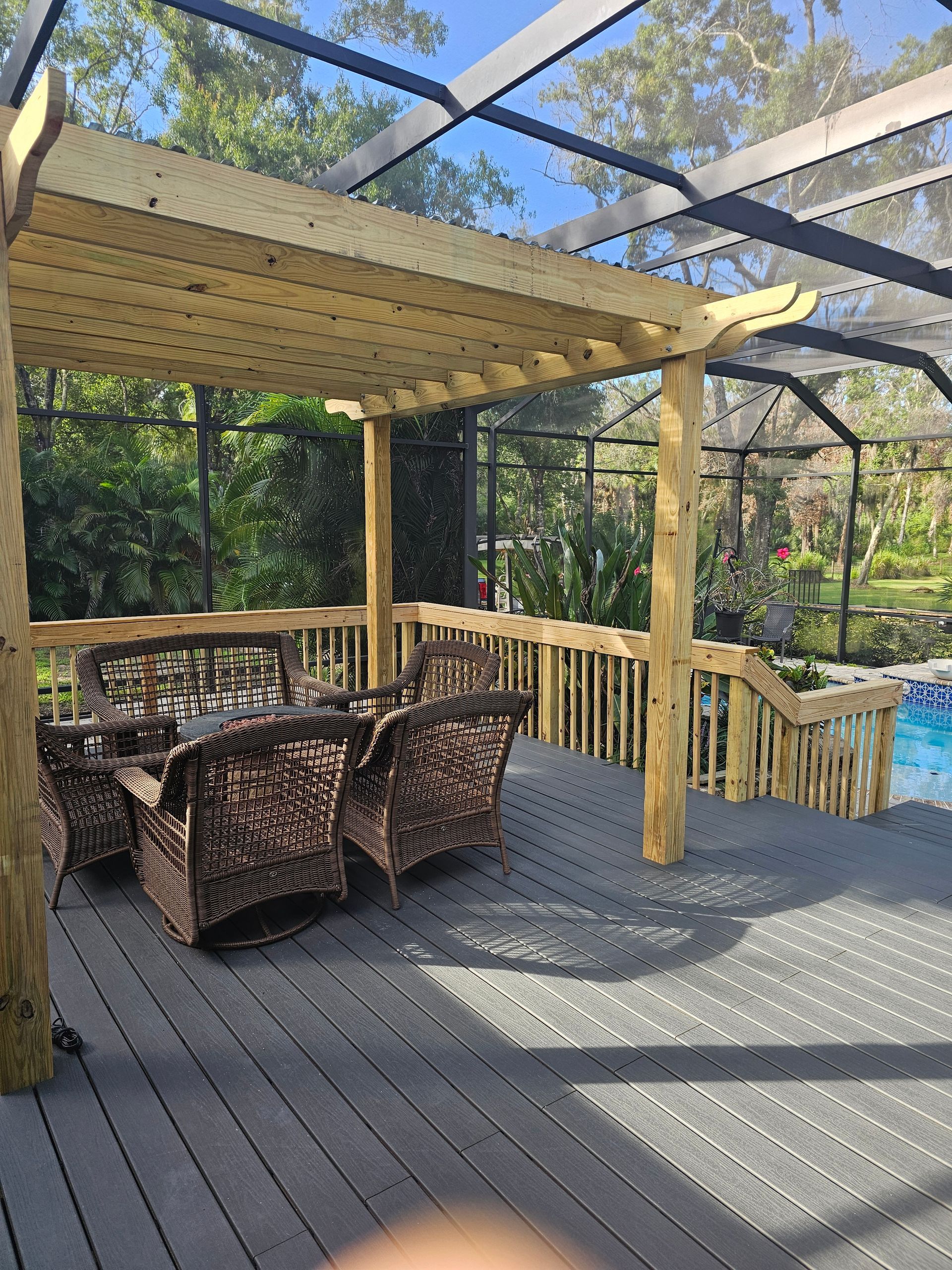 Pergola over a deck with wicker furniture, overlooking a pool enclosed by a screen.