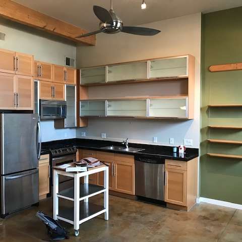 Modern kitchen with stainless steel appliances, light wood cabinets, and green accent wall.