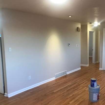 Empty room with tan walls, wood floor, and a can of paint sitting on a bucket.