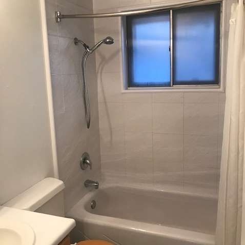 Bathroom with a bathtub, showerhead, and small frosted window; white tiled walls and a partially visible white shower curtain.
