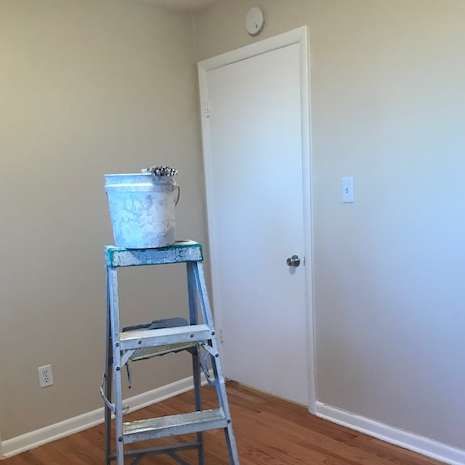 A paint bucket on a step ladder inside a room next to a white door.