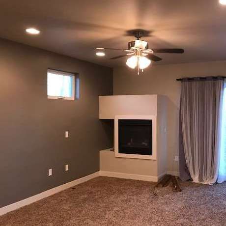 Room with fireplace, small window, brown carpet, gray walls, and light-colored curtains.