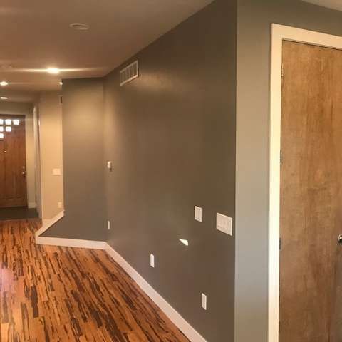 Hallway with hardwood floor, grey walls, and a wooden door. White trim accents.