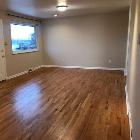 Empty room with hardwood floors, a window, and neutral-colored walls.