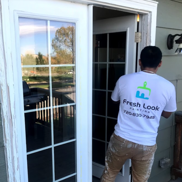 A person in a white Fresh Look Painting shirt is working on a white-framed door.